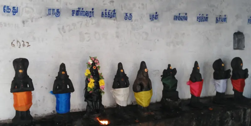 Nine black idols in coloured cloths in a row on a platform