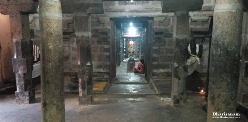 Rough stone pillars in a dim hall, with a lit doorway and the deity visible far ahead in the sanctum.