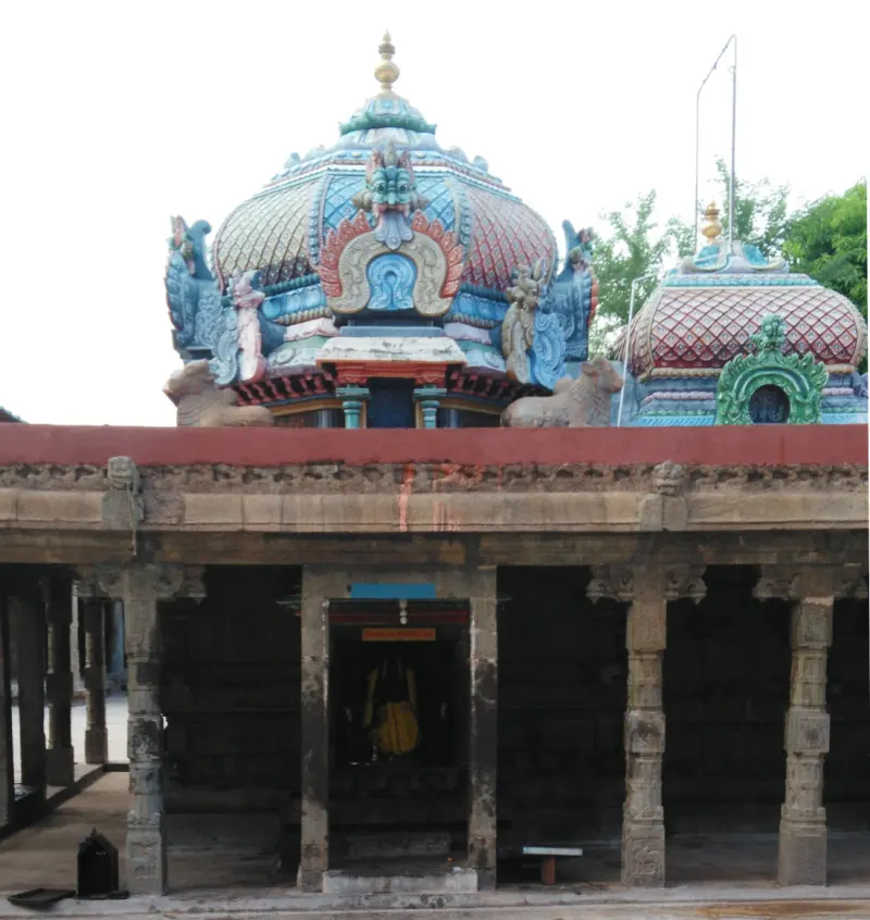 Pillared corridor with a small shrine holding a yellow-clad idol, under two colourful domed roofs