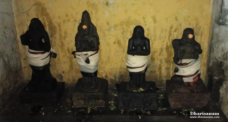 Four small black stone idols in white cloth standing in a row before a yellow wall