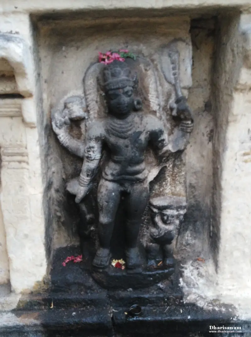 A stone figure with several arms standing in a niche, holding a club, with a flower on its head.
