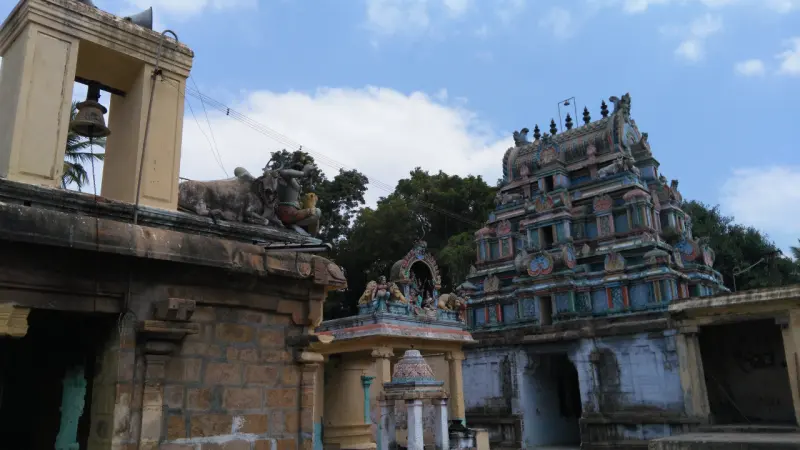 A coloured tower rises beyond a mandapam roof with a bull figure and a bell; a small shrine stands in the middle.