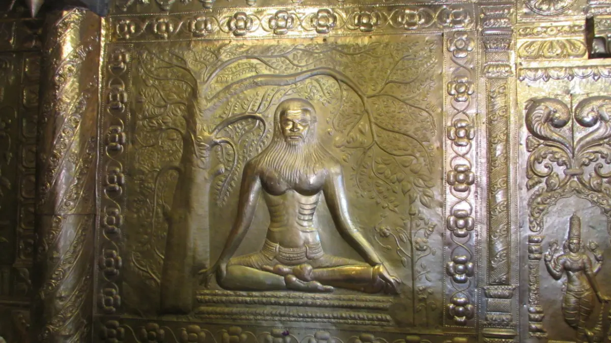 Embossed metal panel showing a bearded yogi seated cross-legged under a spreading tree, framed by floral borders.