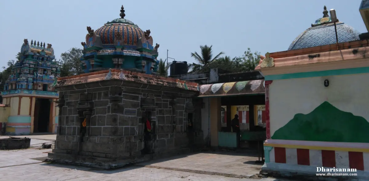 Small shrines with domed roofs and a grey stone wall, with a gopuram visible to the left