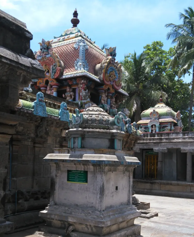 A painted shrine roof rises behind a small stone pedestal with a green sign; another shrine stands to the right.
