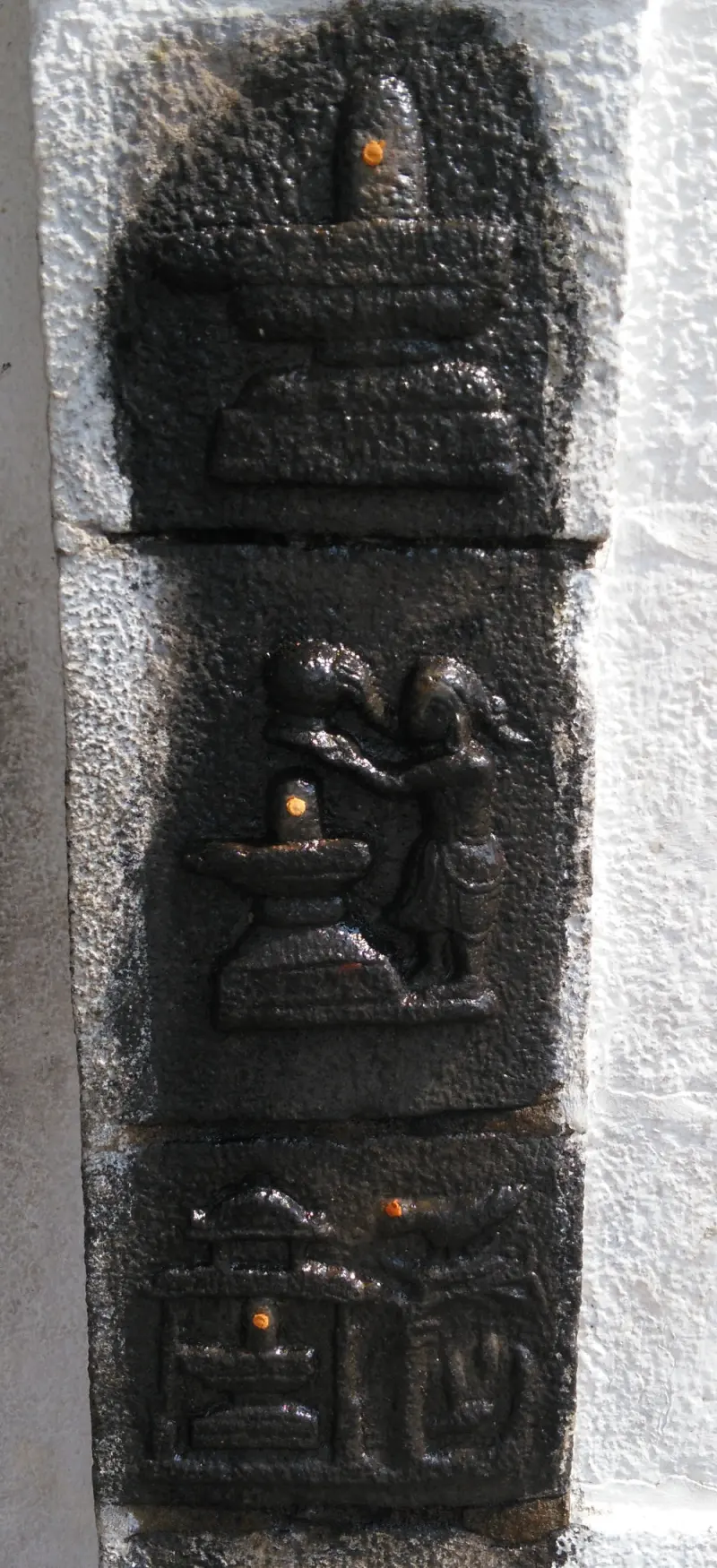 Three dark stone panels showing a lingam, a figure pouring water over a lingam, and a lingam in a small shrine