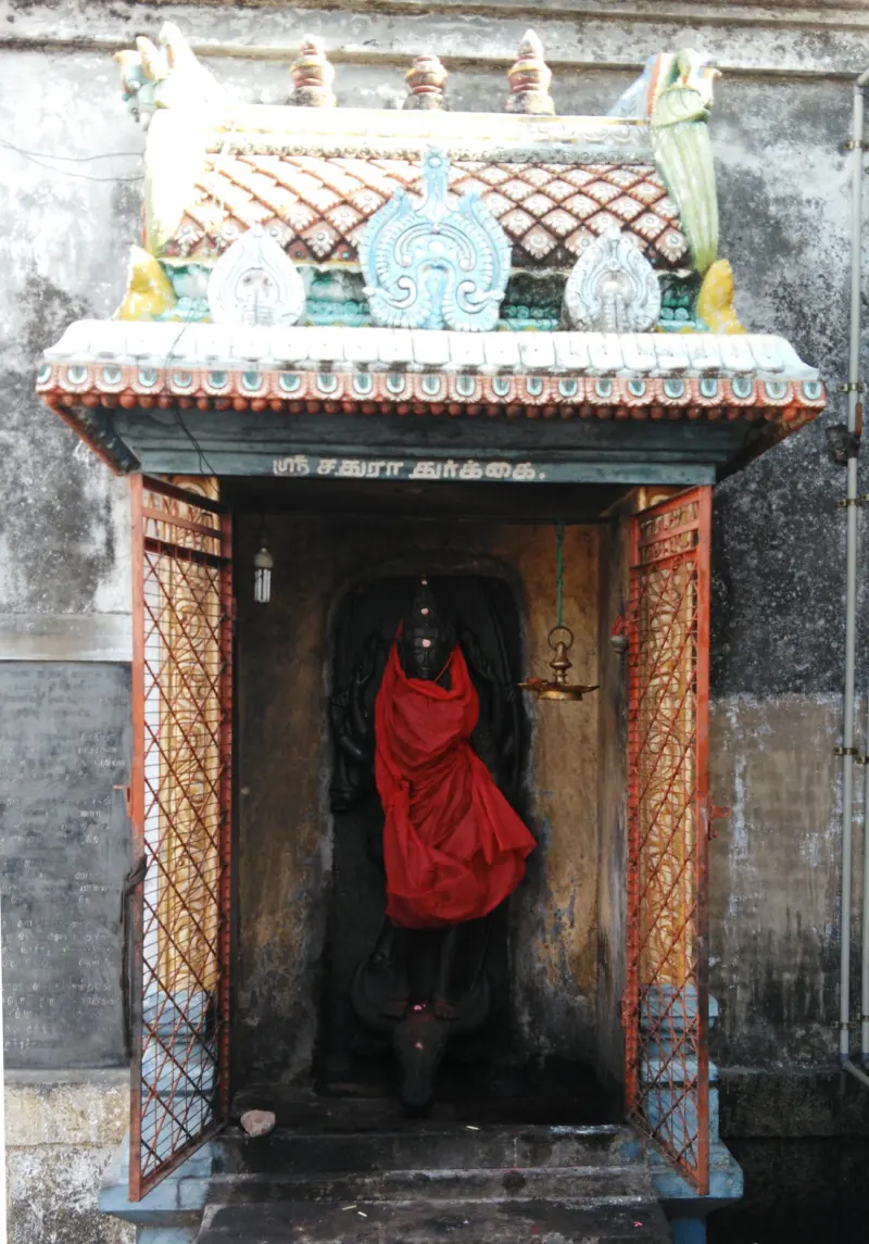 Small shrine with a Tamil name board and a dark stone goddess draped in red