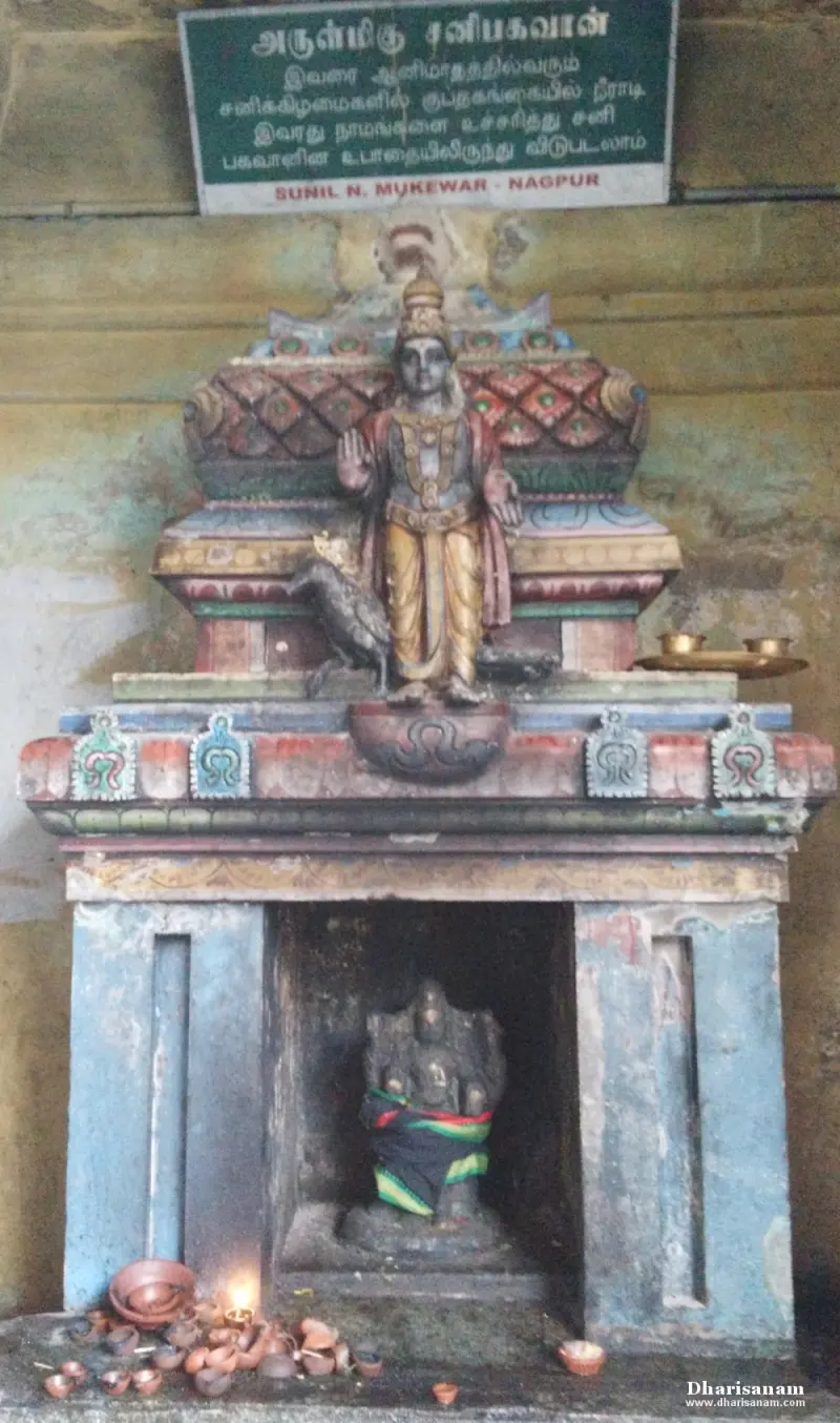 A small blue shrine holding a dark idol, topped by a painted standing figure and a green sign