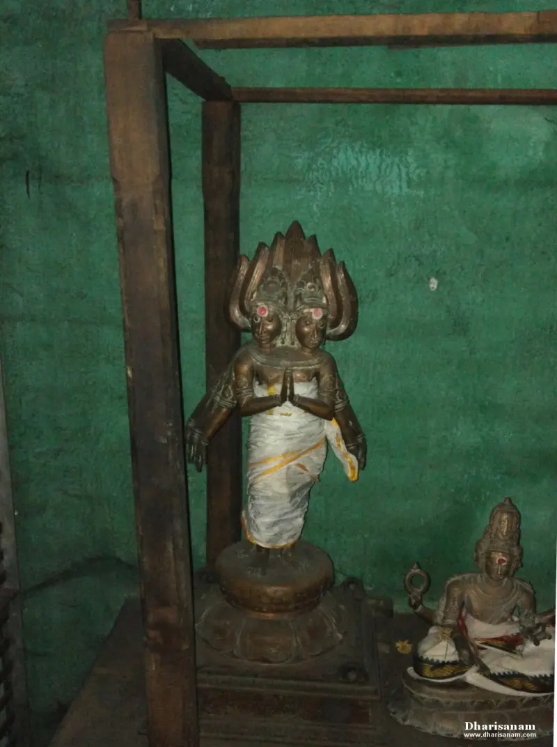 A bronze figure with joined hands, two faces and a flame-shaped crown, beside a smaller seated bronze