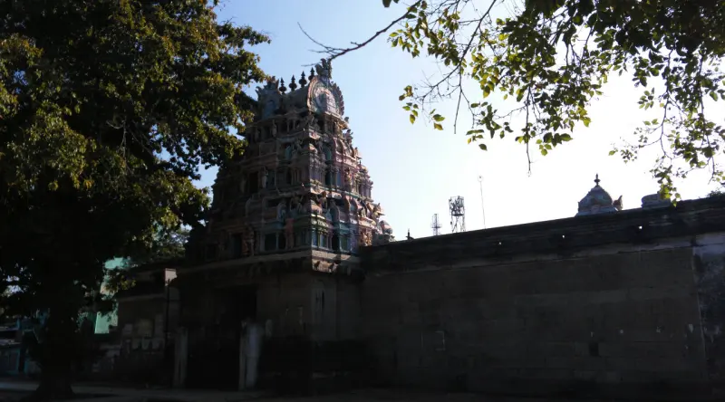 Tiered gopuram behind trees and a long stone compound wall