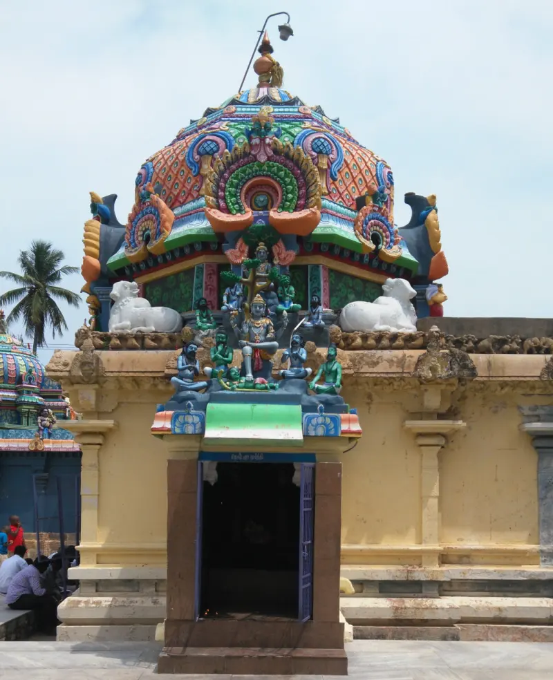 A small yellow shrine with a colourful dome, white bulls and deity figures above its open doorway