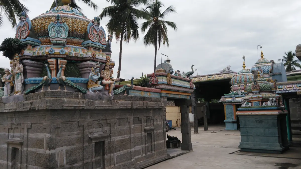 Colourfully painted shrine towers and a stone-walled shrine among palm trees under a cloudy sky.