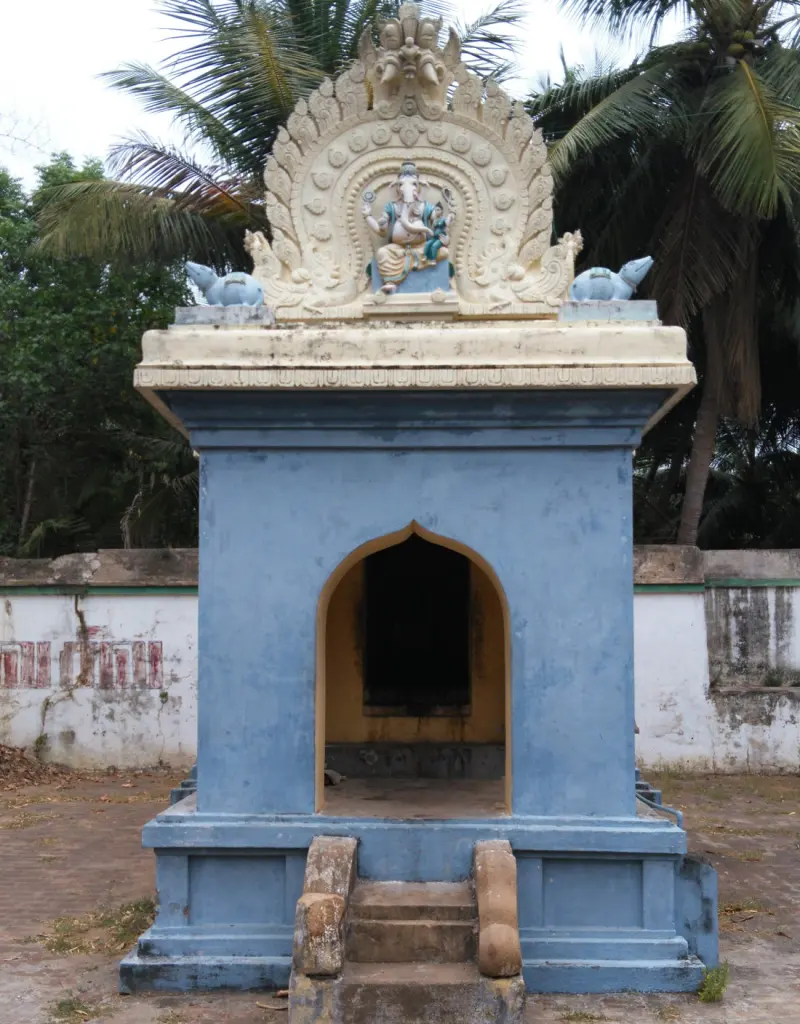 A small blue shrine with an open front, a Ganesha figure above and palm trees behind.