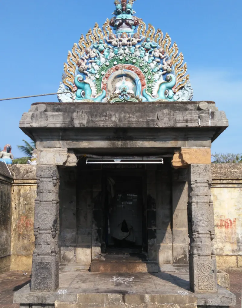 A small stone shrine with a dark doorway and a colourful arched crest above it