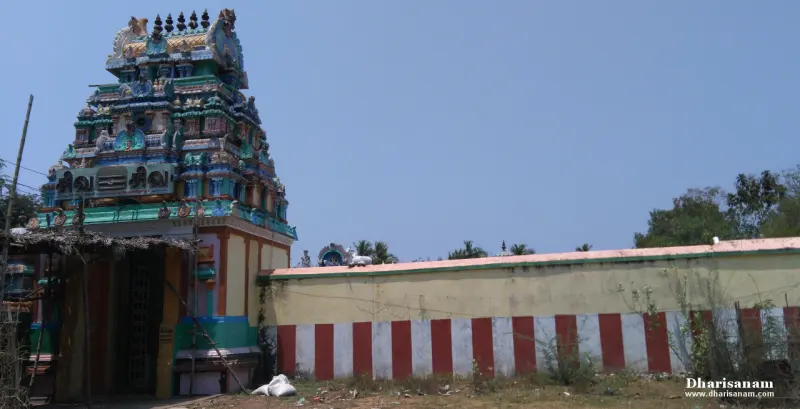 A colourful temple entrance tower beside a long compound wall painted in red and white stripes
