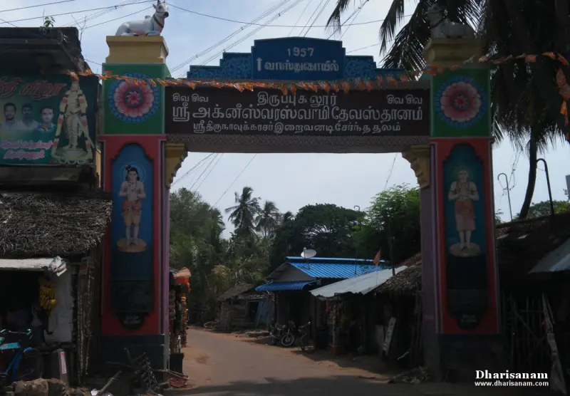 A painted entrance arch with a Tamil name board over a village road, with shops on both sides