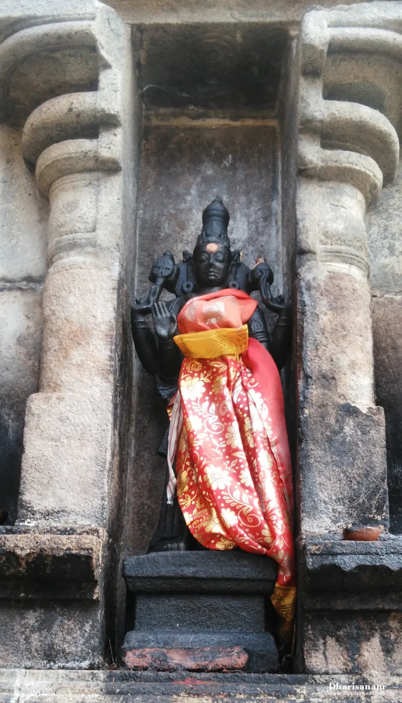 A dark four-armed idol with a tall crown is draped in red and gold silk inside a stone niche