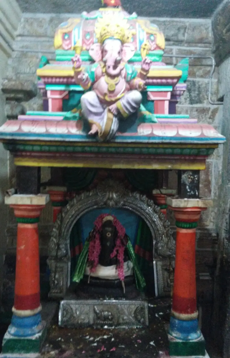 A dark idol with a pink garland sits in an arched niche; a painted Ganapathy figure sits on the canopy above.