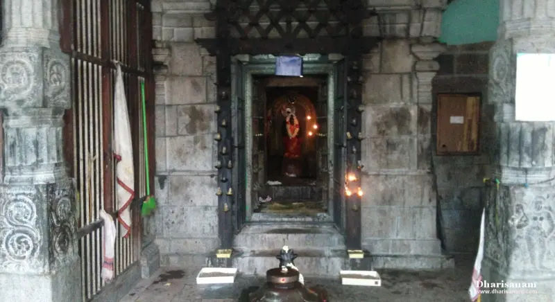A small shrine with a lit lamp inside, seen from the corridor over a bali peetam.
