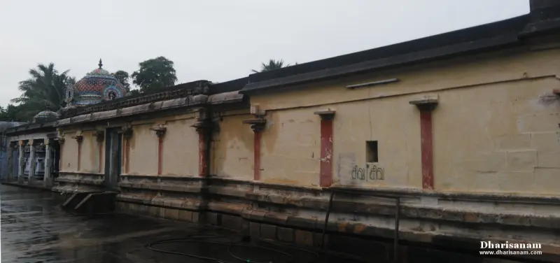 Long cream wall with red pilasters under a grey sky, a domed shrine roof showing beyond the wall