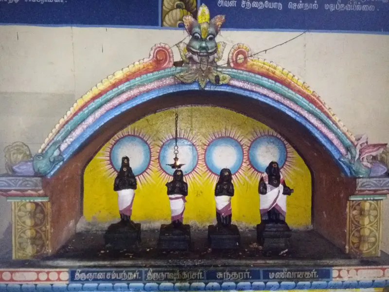 Four dark figures in white cloth stand before painted halos under a rainbow-coloured arch