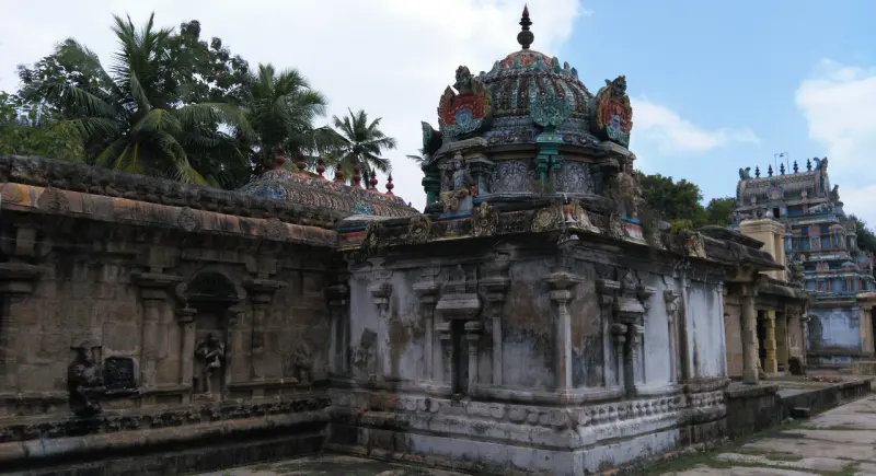 A pale stone shrine with a painted dome beside a long corridor wall; a tiered tower stands in the distance at right.