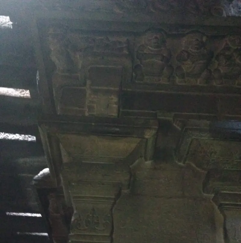 A dimly lit stone beam above a pillar, carved with small seated figures in a row