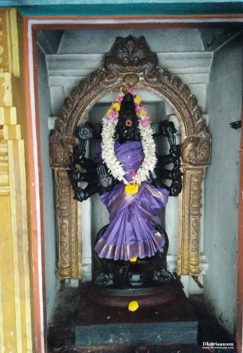 A dark idol with many arms in a purple sari and flower garland, under a carved arch