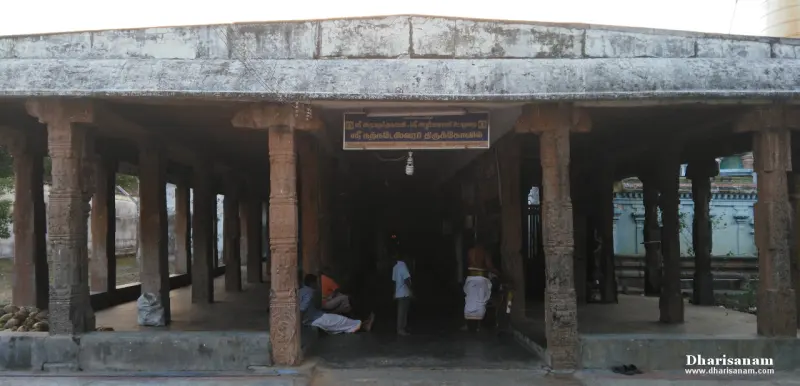 Carved stone pillars hold a flat roof, with a hanging name board and a few people at the back