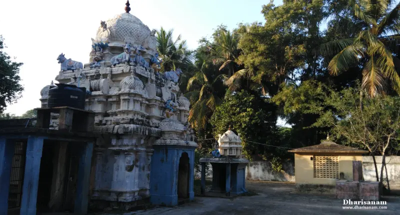 A white tower with bulls on its tiers beside a small blue shrine, with a few shrines and trees in the courtyard