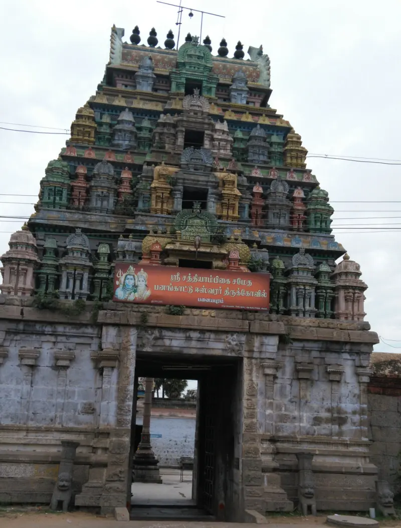 A tall colorful tower over a stone gateway with a Tamil name board