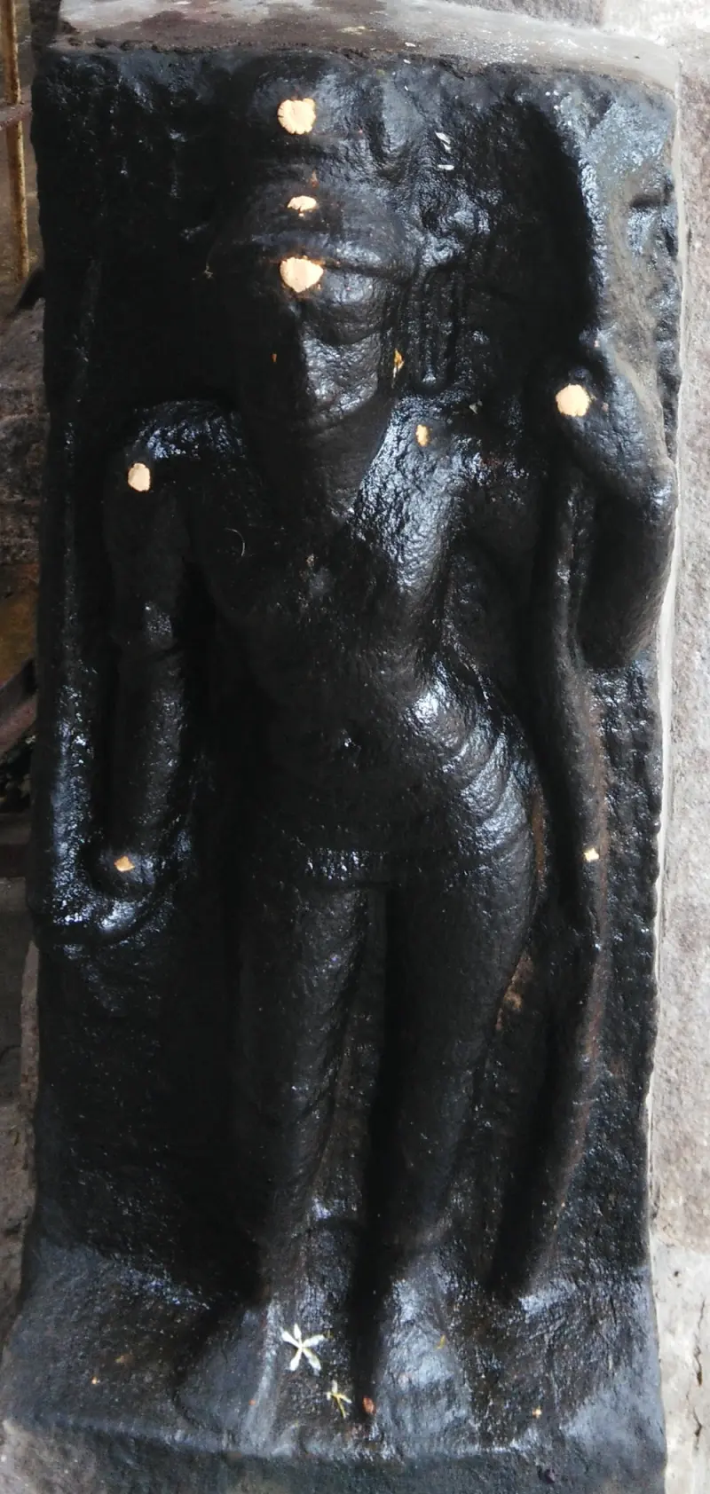 A black stone relief of a standing figure in a niche, with dots of gold on its forehead and chest