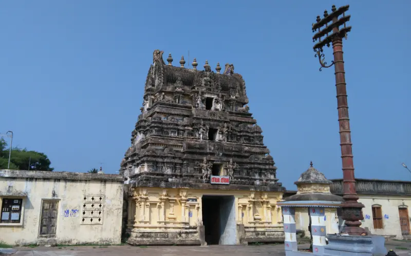 A weathered stone tower over a yellow gateway, with a tall flagstaff to its right under a blue sky.