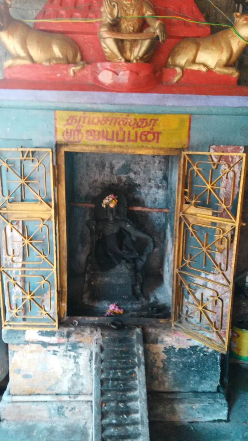 A black seated Iyappan behind yellow grilles under his name board