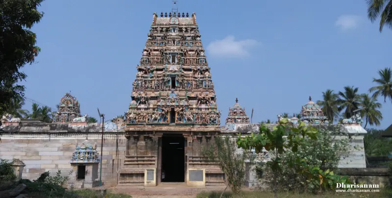 A tiered gateway tower of painted figures rising above a stone wall, with small shrine roofs on either side