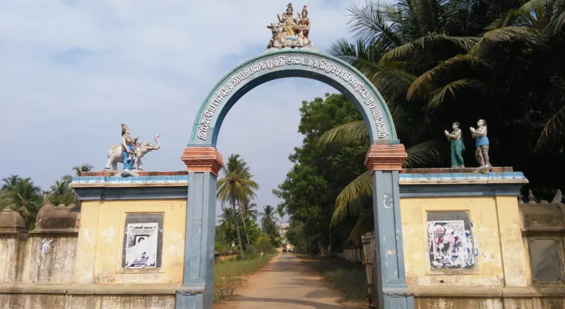 A painted arch with figures on top spans a village road lined with coconut palms