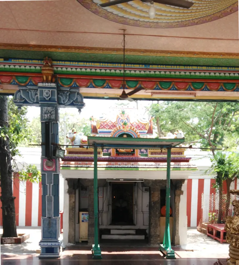 A small shrine with green pillars and a painted roof, framed by a blue painted pillar in front.