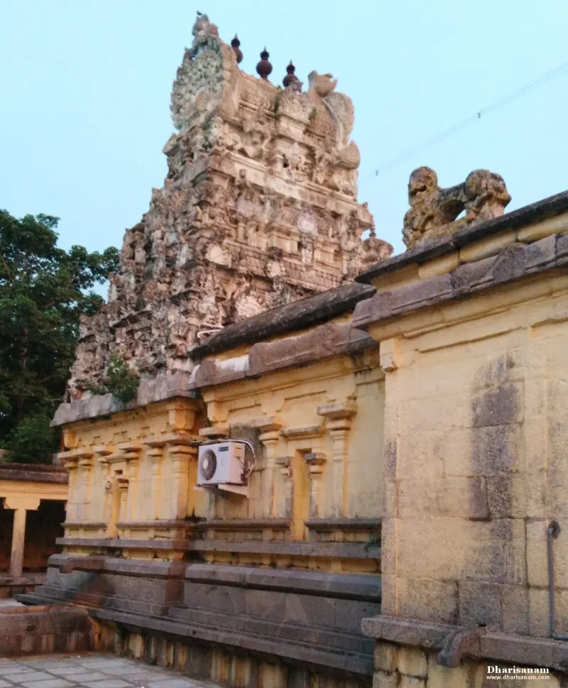 A worn sculpted tower rising behind a yellow-walled hall with a lion carving on the roof edge