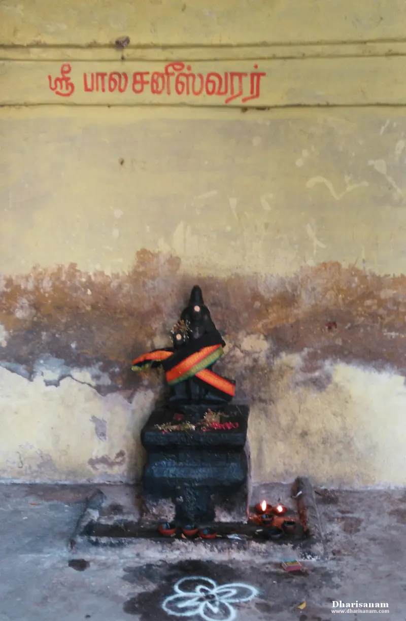 A small dark idol with a striped cloth, lamps burning before it
