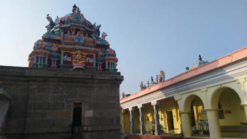 A carved stone tower beside a yellow pillared hall