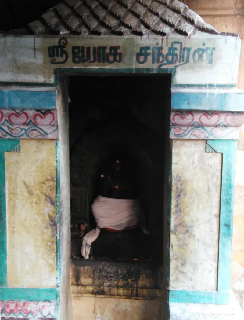 A small painted shrine with Tamil lettering above, holding a dark idol wrapped in cloth