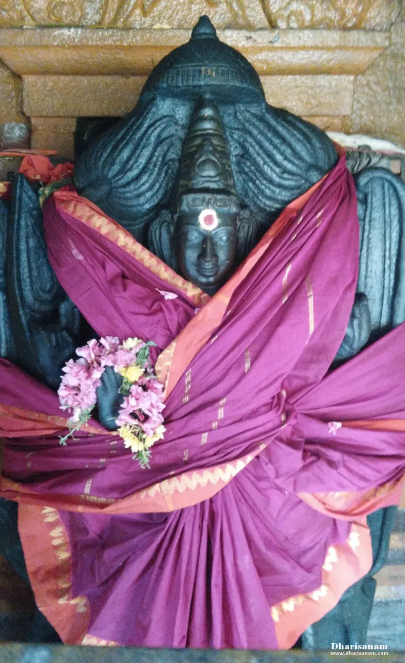 Dark stone idol of a goddess draped in a purple sari and flower garlands