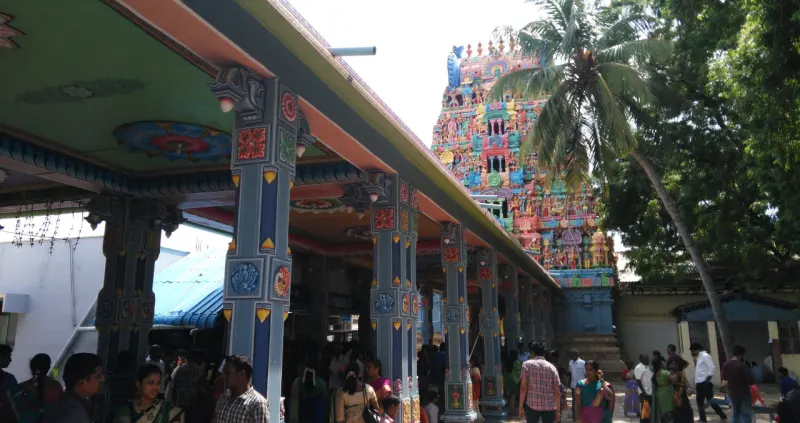Devotees in a painted pillared hall, with a colourful tower and a palm tree behind