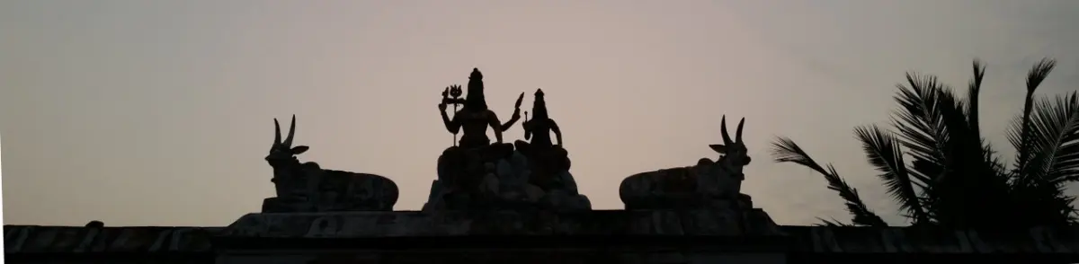 Dark silhouettes of a seated divine couple on a pedestal with a bull on each side, against the evening sky