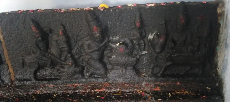 A dark stone relief panel of several figures, with flowers laid along its top edge