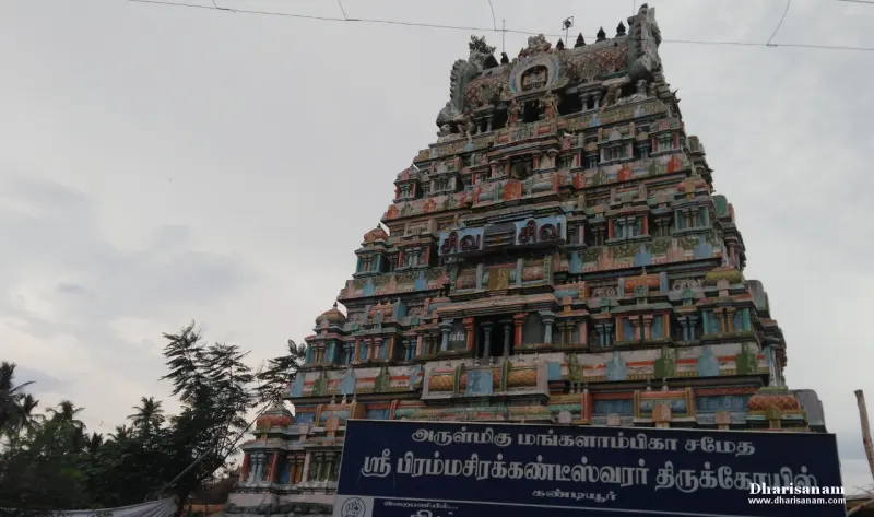 A tall, many-tiered painted tower seen from below, with a blue Tamil name board in front.