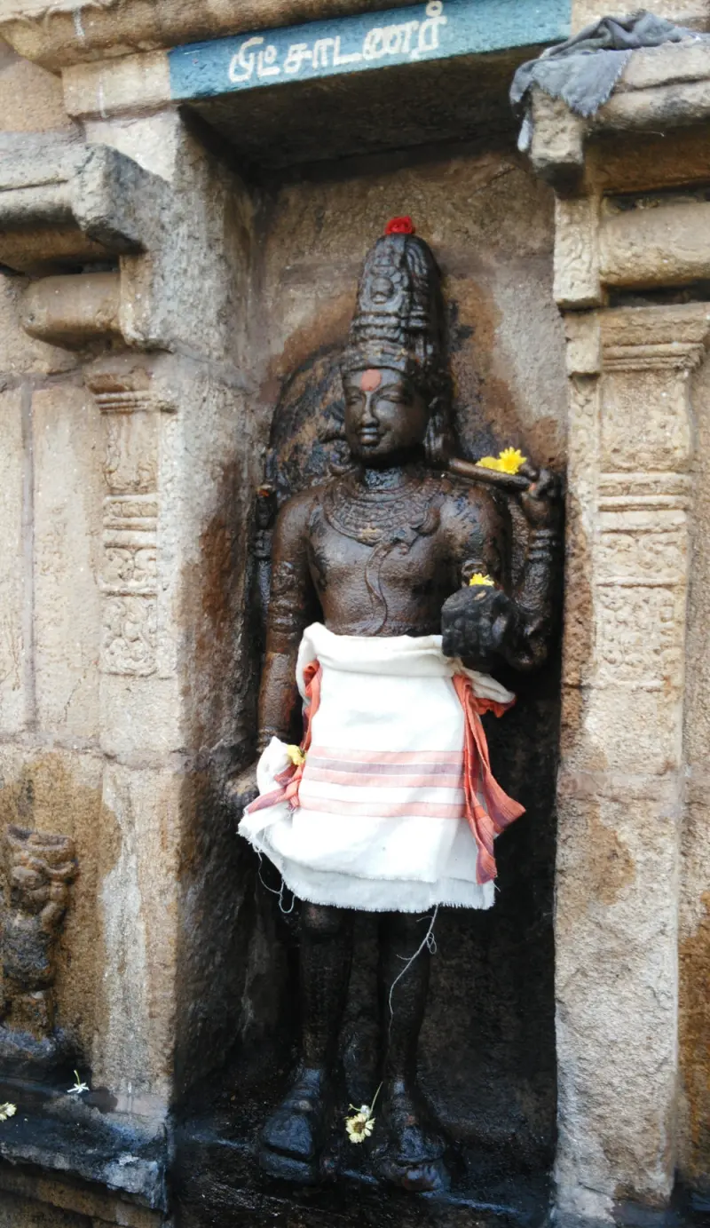 Standing stone figure with a tall crown, wearing a white cloth with a red border, in a wall niche