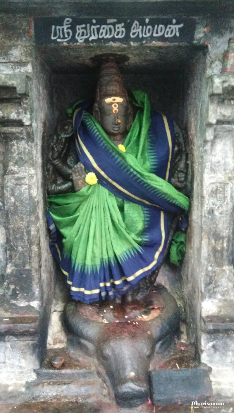 Durgai in a green and blue sari standing in a niche under a name board, on a buffalo head