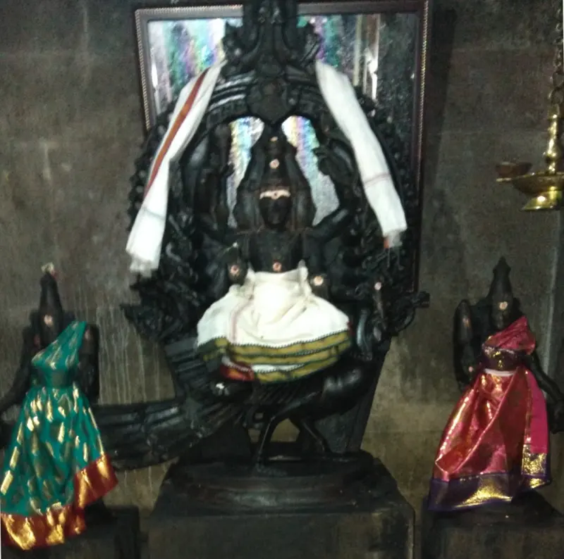 A dark stone deity flanked by two attendant figures in silk