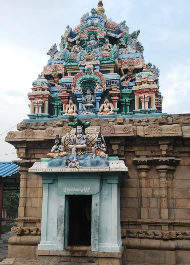 A shrine with a Tamil name board and a painted tower, with Dakshinamurthy and two devotees above the door.